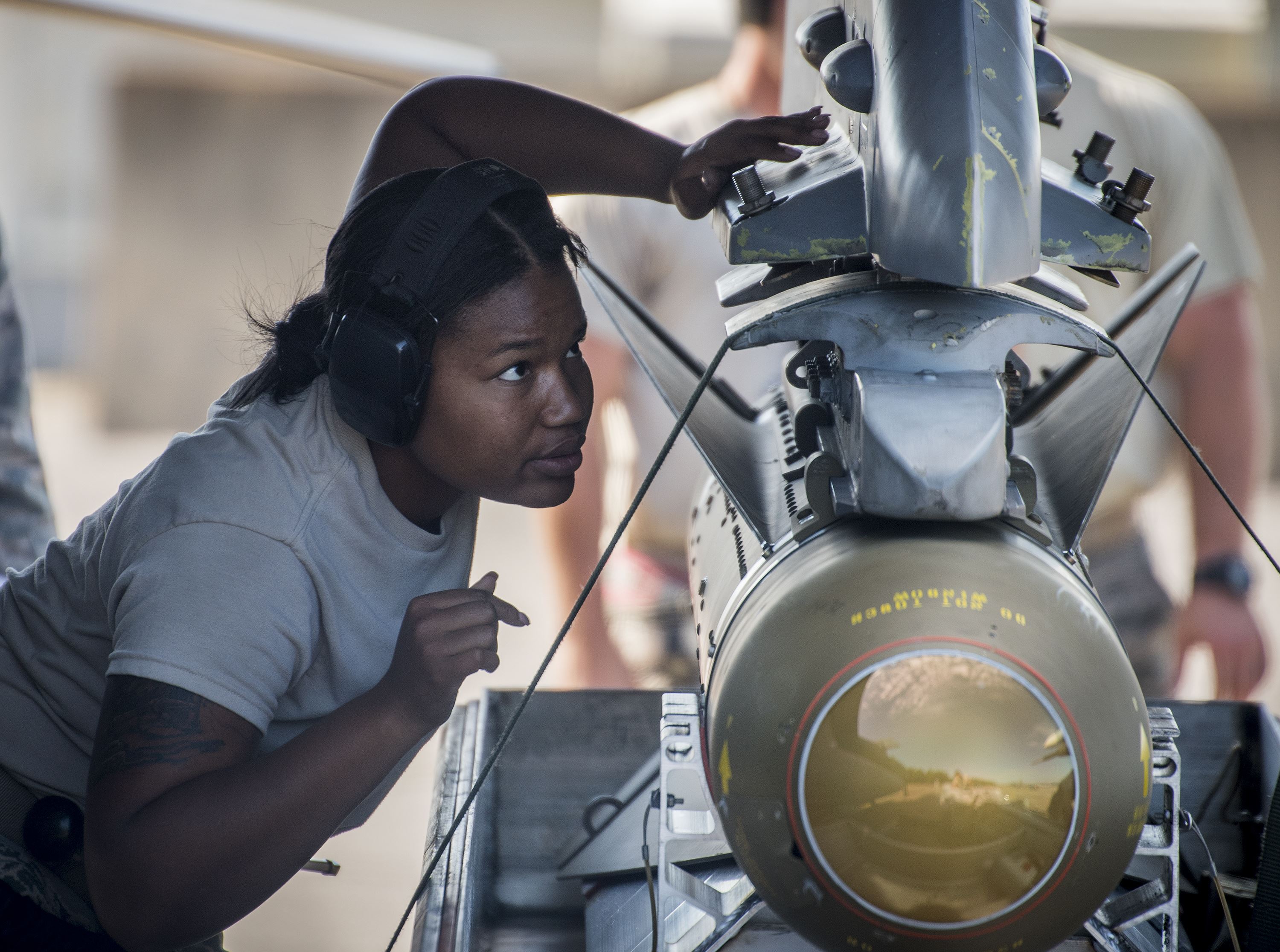 Air Force member inspects a bomb being mounted to a fighter jet.