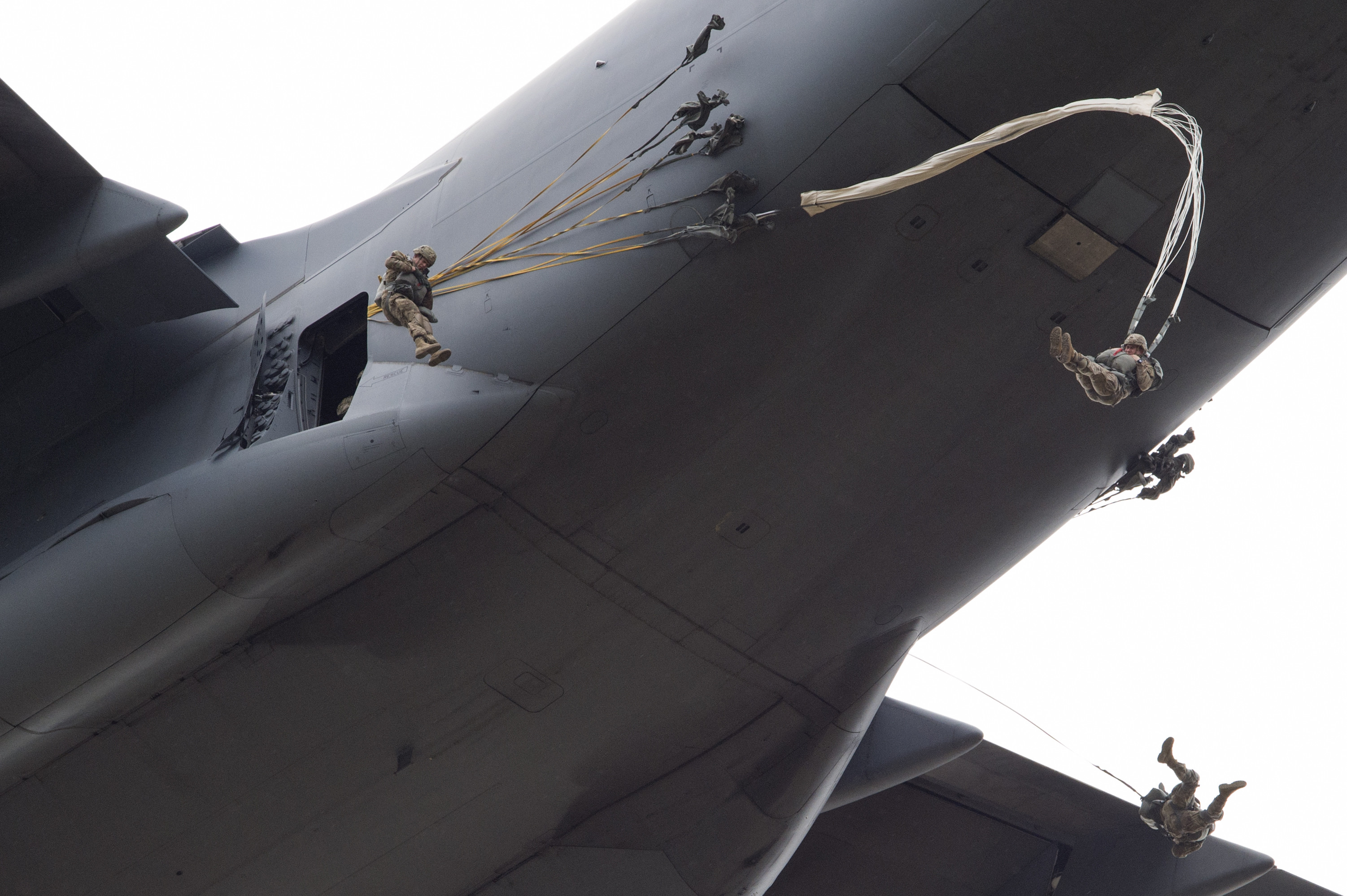 US military members jumping out of a cargo plane and opening parachutes